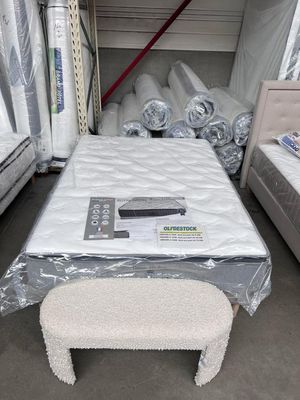 Matelas Royal Hôtel présenté sur son sommier, entouré de matelas roulés et d’un lit avec tête de lit capitonnée