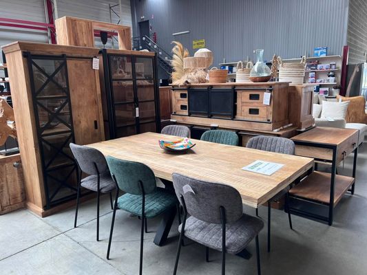 Table de repas en bois et chaises dépareillées devant des vitrines et un buffet