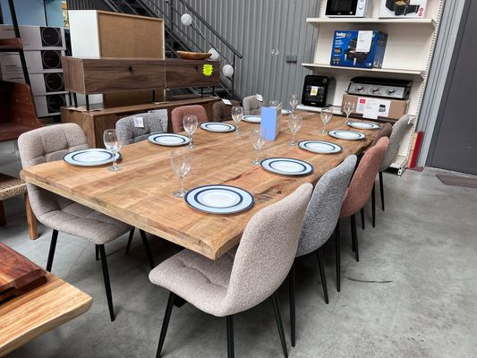 Table de repas en bois dressée avec assiettes et verres, chaises en tissu